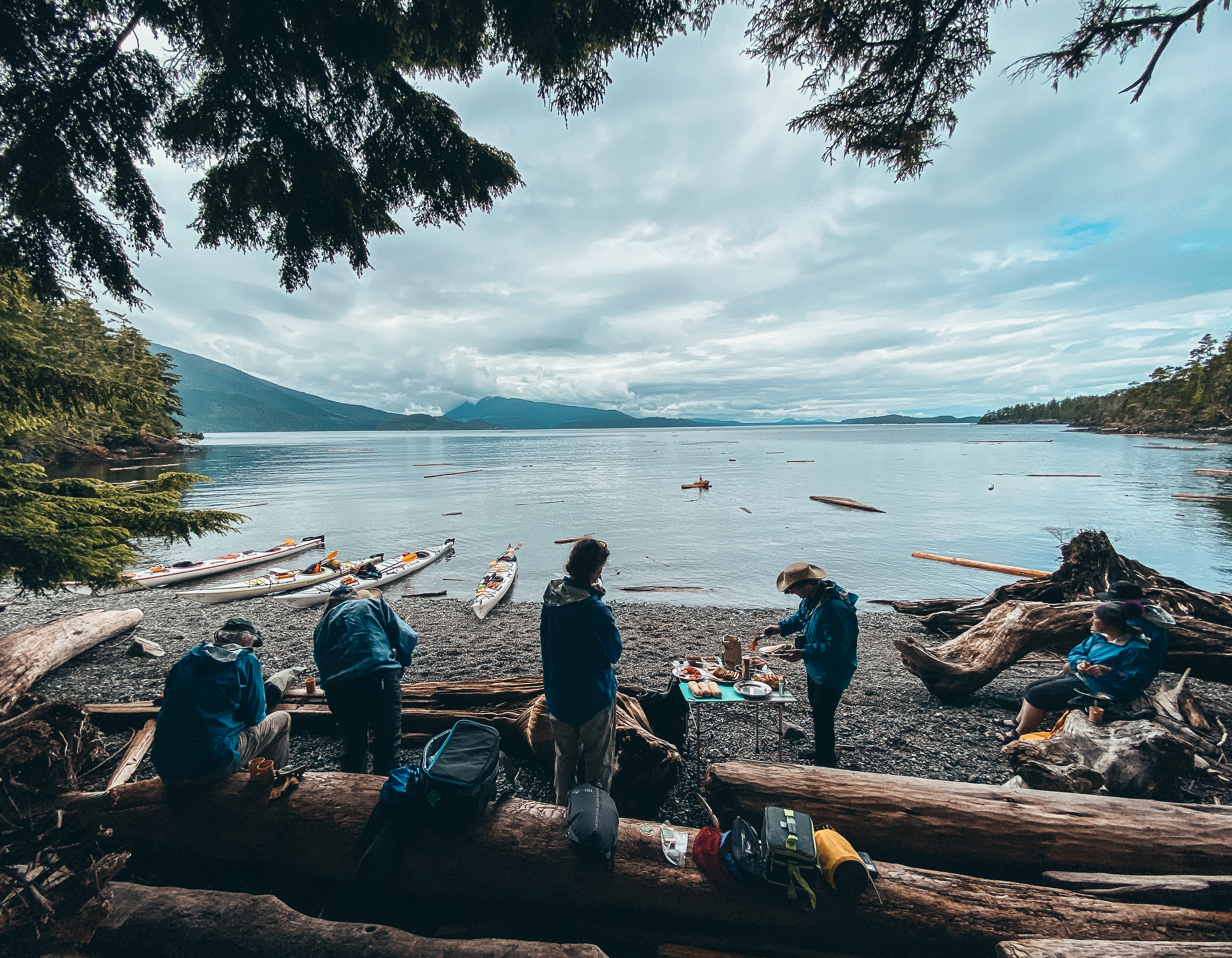 people standing on a beach with kayaks in the back in telegraph cove